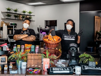Two cashiers with face masks standing in the cafe with merchandise.