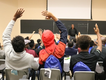 Students raising their hands in a classroom.