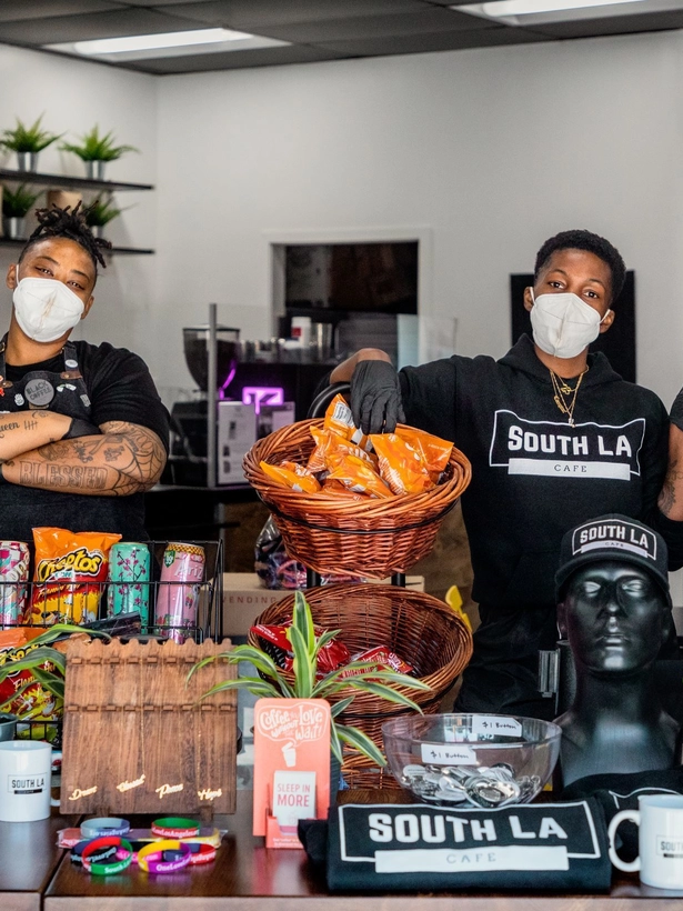 Two cashiers with face masks standing in the cafe with merchandise. 